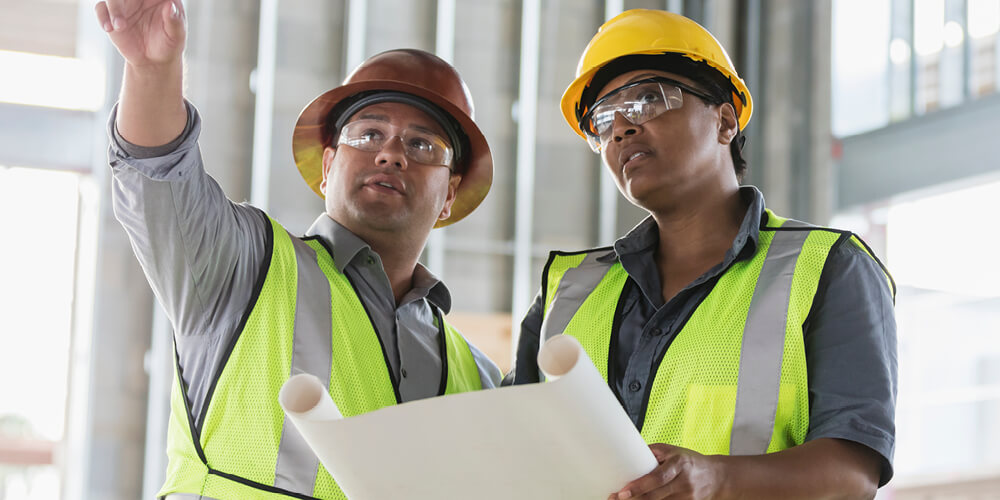 Two workers in green safety vests and hard hats.