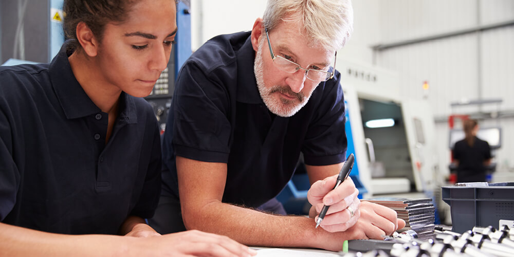 a man and woman looking at at a document in a manufacturing facility.