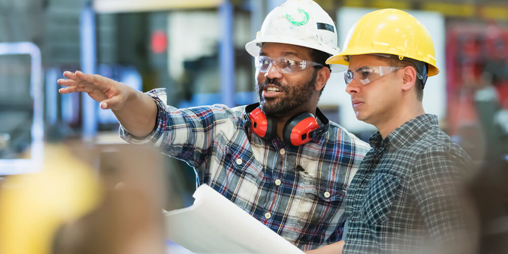 Two men on a worksite wearing hard hats and safety glasses.