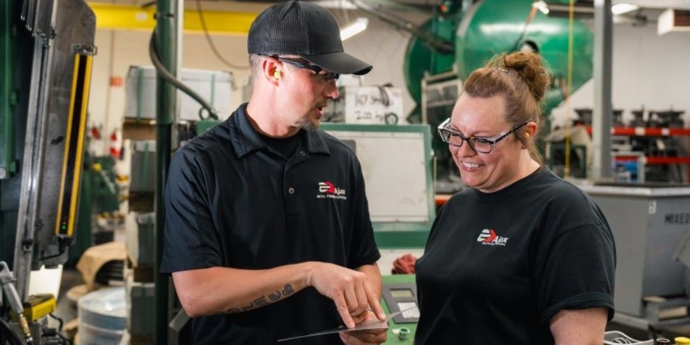 a man and woman looking at at a document in a manufacturing facility.